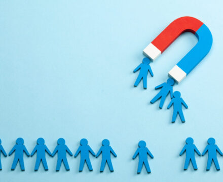 A red and blue horseshoe magnet attracts several blue paper-cutout people from a row of similar paper figures on a light blue background.